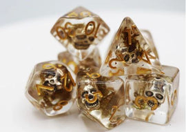 A close-up view of a Silver Pirate Skull RPG Dice Set, featuring translucent dice with embedded skull designs and gold lettering for numbers. The set includes various polyhedral dice, ideal for tabletop RPGs, adding a unique aesthetic to gameplay.