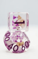 A close-up view of a Purple Koi Fish RPG Dice Set by Foam Brain Games. The set includes a translucent purple die featuring intricate koi fish designs and numbers, perfect for tabletop gaming enthusiasts. The dice are decorated with shades of purple and natural textures, adding a unique touch to gameplay.