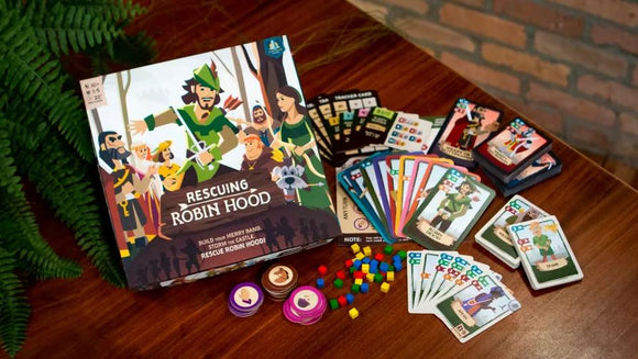Rescuing Robin Hood board game from CASTILLO GAMES displayed on a wooden table. The game box features colorful artwork with characters from the Robin Hood legend. Surrounding the box are various game components, including character cards, tracking cards, tokens, and colorful game pieces, creating an inviting setting for family and friends to enjoy together.