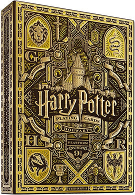 Harry Potter-themed playing cards packaging showcasing intricate designs featuring Hogwarts castle, house crests, and themed illustrations, primarily in yellow and gold colors. Crafted by Theory 11, this collectible deck is perfect for fans of the wizarding world.