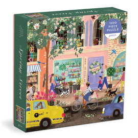 Spring Street jigsaw puzzle by Galison, featuring a vibrant, illustrated street scene with a flower shop, cyclists, pedestrians, and iconic yellow taxis. The puzzle contains 1000 pieces and is perfect for puzzle enthusiasts and art lovers alike.