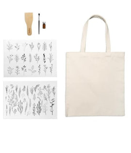 Kikkerland Design Inc Image Transfer Tote Bag DIY kit. Features a blank canvas tote bag alongside two sheets with various botanical prints, a wooden burnishing tool, and a small bottle of transfer medium, ideal for personalized projects.