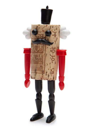 Corkers Classics Nutcracker designed by Monkey Buisness Design. The quirky nutcracker figure features a cork body with expressive eyes, a black top hat, a curled mustache, and colorful arms made of red and white plastic. It stands on a black base, showcasing a playful and unique design.