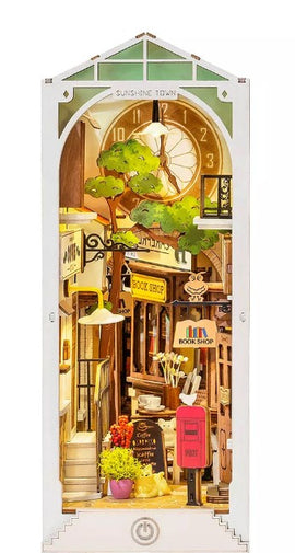 The Sunshine Town DIY Book Nook by Robotime features a charming miniature scene including a bookshop, vibrant greenery, and a nostalgic clock. The detailed design invites creativity, making it a perfect DIY kit for craft enthusiasts.