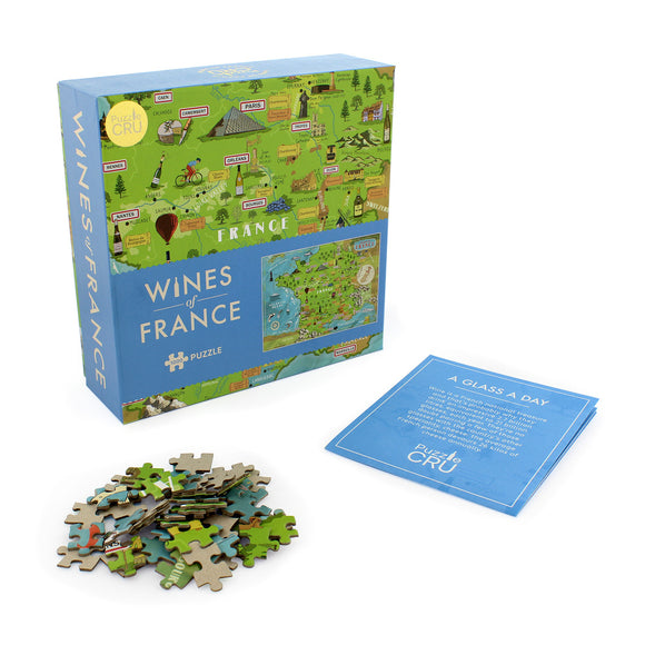 Wines of France jigsaw puzzle by Ginger Fox, featuring a colorful map of France with wine regions, landmarks, and fun illustrations. The box shows vibrant graphics and includes a card with trivia. Puzzle pieces are scattered in front.
