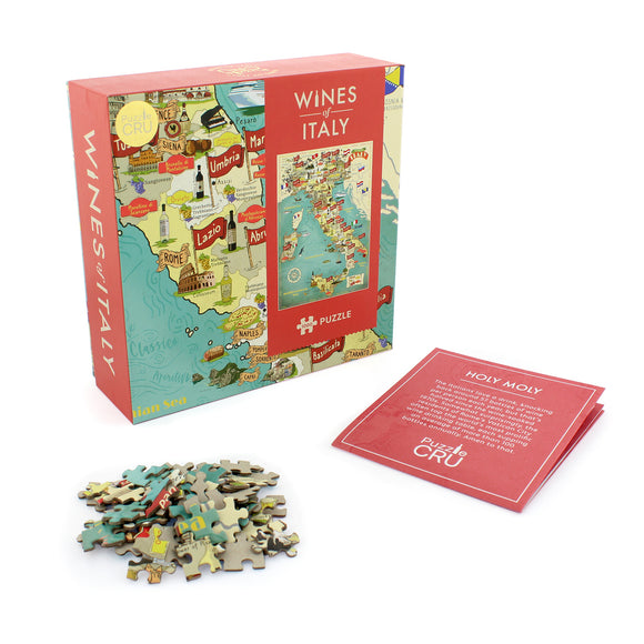 Wines of Italy jigsaw puzzle by Ginger Fox, featuring a colorful map of Italy with notable wine regions. The box is open, showing scattered puzzle pieces and an informational card titled 'Holy Moly' that describes Italian wine culture.