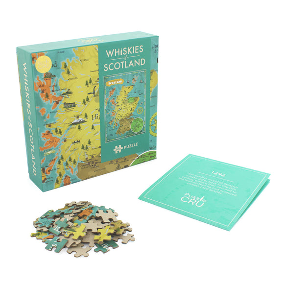 Whiskies of Scotland jigsaw puzzle by Ginger Fox, featuring a colorful map of Scotland highlighting various whisky regions. The puzzle includes several jigsaw pieces scattered around the box, with a booklet nearby detailing whisky facts.