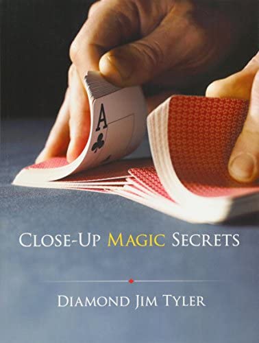 A close-up view of hands skillfully manipulating playing cards, specifically showing a card with an Ace of Spades. The book titled 'Close-Up Magic Secrets' by Diamond Jim Tyler is prominently displayed, focusing on techniques and tricks for mesmerizing card magic.