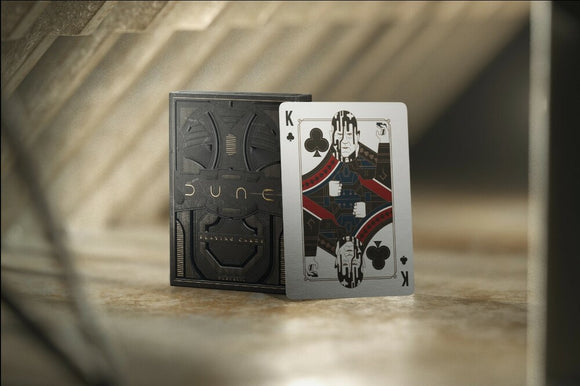 Dune Playing Cards by Theory 11 displayed with the pack partially open to reveal a King of Spades card. The card features intricate designs inspired by the Dune universe, set against a backdrop of soft, diffused lighting.