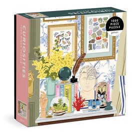 The Curiosities jigsaw puzzle by Galison features a vibrant illustration of a cozy interior adorned with various curiosities, including a bouquet of yellow flowers, a glass terrarium, framed butterfly artworks, and a vintage camera. This 1000-piece puzzle showcases a charming display that invites creativity and exploration.