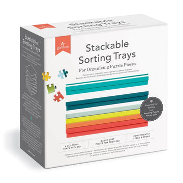 A box of Stackable Sorting Trays by Galison, designed for organizing jigsaw puzzle pieces. The packaging features colorful trays in various shades, along with a lid. It highlights six trays that stack easily for convenient storage and sorting, ensuring that puzzle pieces are kept safe and organized while working on puzzles.