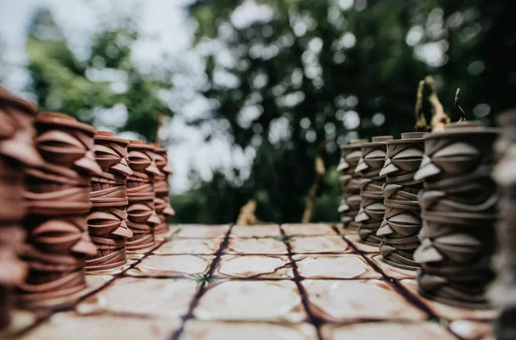 TacTiki game from DRAWLAB GAMES featuring an outdoor setting. The game board is visible with stacked piece formations arranged in two distinct colors, creating a visually striking contrast. Lush greenery in the background enhances the game's vibrant and fun atmosphere, perfect for family and friends.