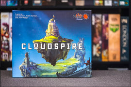 The board game Cloudspire by Chip Theory Games features a detailed illustration of a floating island landscape on the box cover. The title 'CLOUDSPIRE' is prominently displayed in bold letters. Smaller text credits the game creators: Josh Carlson, Adam Carlson, and Josh Wiegus.