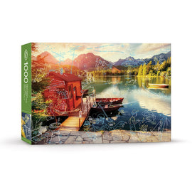 The LIVING LA VIDA LAKE (AHHH) jigsaw puzzle box from FRED Distribution Inc. features a picturesque lakeside scene with a vibrant sunset over the mountains, a red lodge, and whimsical sketches of outdoor activities. The puzzle contains 1000 pieces, inviting enthusiasts to recreate this serene landscape while engaging with playful doodles.