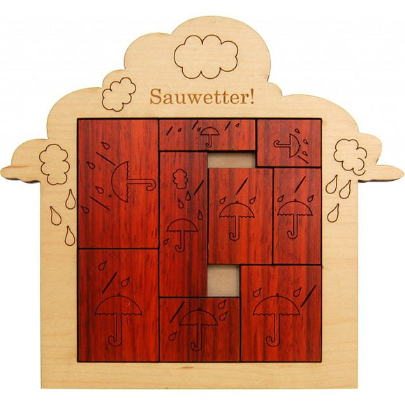 A wooden mechanical puzzle titled 'Stormy Weather (Sauwetter)' designed by Jean Claude. The puzzle features a playful design of umbrellas and raindrops, crafted from wood with engraved illustrations. The puzzle pieces are arranged within a cloud-shaped frame, showcasing a rich brown color.