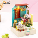 A beautifully crafted DIY miniature flower shop model kit named 'Flower Leisure Time DIY' by Guangzhou Hongda Craft Co., Ltd. The model features intricate details, including a blue wall, red window, potted flowers, and a small table with a lamp. The scene is vibrant and inviting, perfect for hobbyists who enjoy crafting.