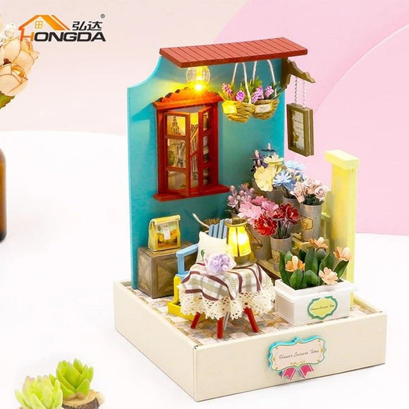 A beautifully crafted DIY miniature flower shop model kit named 'Flower Leisure Time DIY' by Guangzhou Hongda Craft Co., Ltd. The model features intricate details, including a blue wall, red window, potted flowers, and a small table with a lamp. The scene is vibrant and inviting, perfect for hobbyists who enjoy crafting.