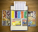 Open box of the game 'First Rat' by Pegasus Spiele showing organized game components including colorful tokens, cards, and game board. The box features sections filled with various game pieces such as dice, cards, and coins, as well as a player score sheet.