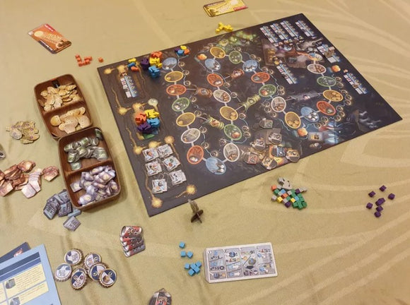 The game 'First Rat' by Pegasus Spiele, featuring a vibrant game board with colorful tokens, cards, and various game pieces scattered around. The board displays intricate paths and game mechanics, showcasing a rich design suitable for engaging gameplay. The scene captures a creative and social atmosphere, ideal for family game nights.