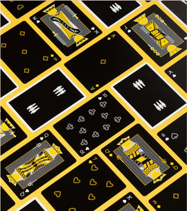A vibrant card deck featuring a unique design with black background and yellow accents. The cards show various traditional suits and royal figures, perfect for game nights. Designed by Art of Play, this deck combines playfulness and artistry for an engaging gaming experience.