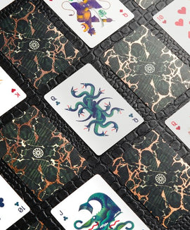 A detailed image of the Forbidden Forest Card Deck featuring beautifully illustrated playing cards. The cards showcase intricate designs with mythical creatures and vibrant colors set against a dark, textured background. Various card values are visible, enhancing the enchanting theme of the deck.