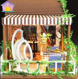The Rainbow Cafe DIY kit by Guangzhou Hongda Craft Co., Lt features a beautifully designed miniature cafe scene. It includes a cozy outdoor seating area adorned with lush greenery, a stylish hanging chair, and a decorated table with a miniature vase and drink. Perfect for craft enthusiasts, this DIY kit invites creativity and adds charm to any space.