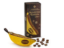 Bananagrams Signature Edition game featuring a banana-shaped pouch filled with letter tiles and a rectangular box showcasing the game name. The box has elegant gold detailing and a glossy finish, and the tiles display various letters.