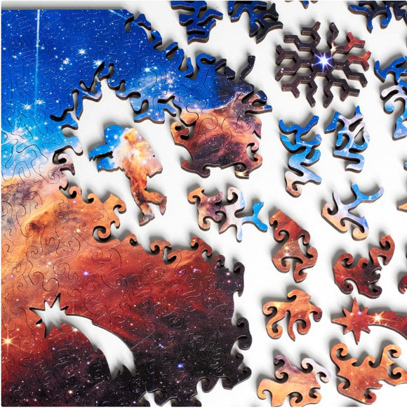 A colorful jigsaw puzzle featuring Cosmic Cliffs Infinite Galaxy design by Nervous System. The image shows vibrant space imagery with pieces in various shapes, including an astronaut and cosmic elements, waiting to be assembled.