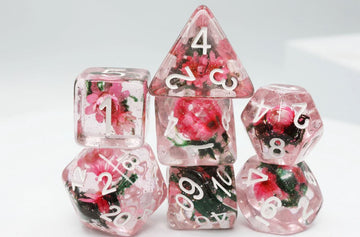 A beautifully crafted set of Carnation Love RPG dice featuring delicate pink flowers encased in transparent resin. The set includes various shapes such as d20, d12, d10, d8, and d6, each displaying vibrant floral designs and clear white numbers for readability. Perfect for enhancing your tabletop gaming experience with a touch of elegance.