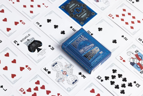 A deck of Bicycle Back to the Future playing cards displayed on a table. The blue card box features iconic imagery from the popular film franchise. Surrounding the box are various playing cards showing vibrant designs, including hearts, clubs, and special illustrations that celebrate the time-traveling theme of the series. This collectible card deck combines nostalgia with classic card game fun.