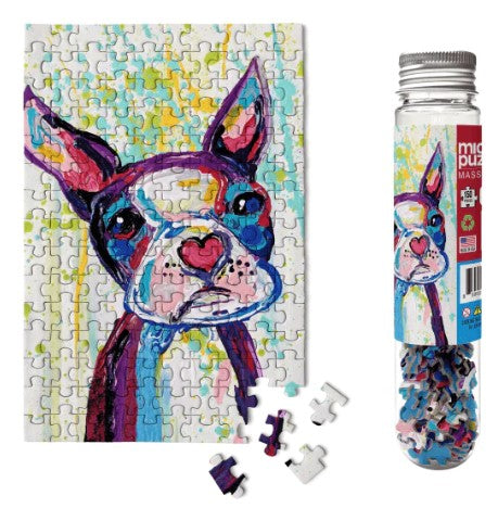 Heart Nosed Ned Micropuzzle by Micro Puzzle displayed with completed jigsaw puzzle illustration of a colorful dog with a heart-shaped nose. The image shows the puzzle pieces scattered and the puzzle in a decorative tube.