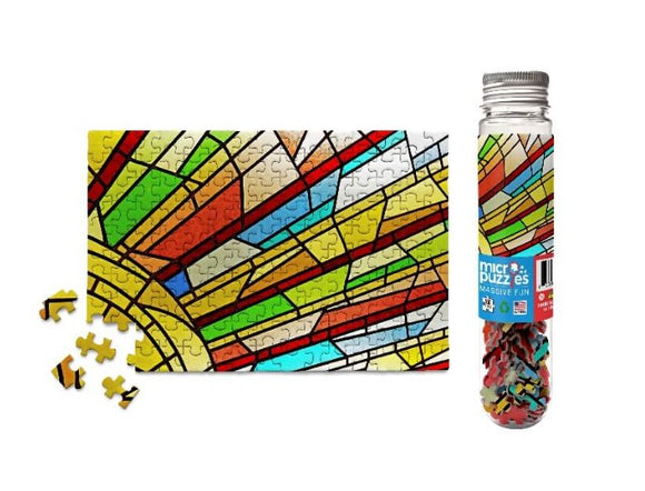 Colorful stained glass window design jigsaw puzzle with vibrant pieces scattered around. The puzzle showcases intricate patterns with reds, greens, and yellows, reflecting a sunlight effect. A clear container filled with additional jigsaw pieces is shown beside the completed segment.