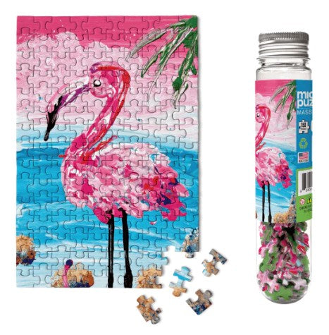 A vibrant Flamingo Micropuzzle by Micro Puzzle displayed alongside its packaging. The completed jigsaw puzzle features a colorful flamingo against a blue background with hints of pink and greenery. Several pieces are scattered nearby, showcasing their intricate designs. The puzzle is housed in a clear tube for easy storage and portability, making it a charming gift for puzzle enthusiasts and bird lovers alike.