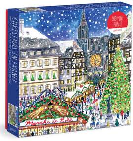 Christmas in France jigsaw puzzle by Michael Storrings, featuring a vibrant and festive winter scene with a Christmas market and snow-covered streets. The puzzle contains 500 pieces and showcases charming architecture, a large decorated Christmas tree, and bustling holiday shoppers.