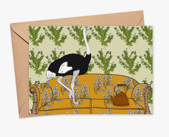 A whimsical standing invitation card featuring an ostrich balancing on a vintage yellow sofa. The background is adorned with leafy green patterns, creating a playful and artistic design. The card is nestled in a kraft envelope.