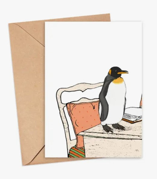 A whimsical greeting card featuring an illustration of a penguin standing on a table. The penguin is positioned next to a stack of books on a white tablecloth. The background showcases an elegant chair with pink upholstery, complementing the playful design. The card is set against a brown kraft envelope.