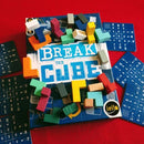 Break the Cube game by Iello, featuring a blue game box with the title prominently displayed in white and light blue letters. Colorful, geometric wooden pieces in various shapes and colors are scattered around the box, alongside game cards with letters and numbers on a blue background.