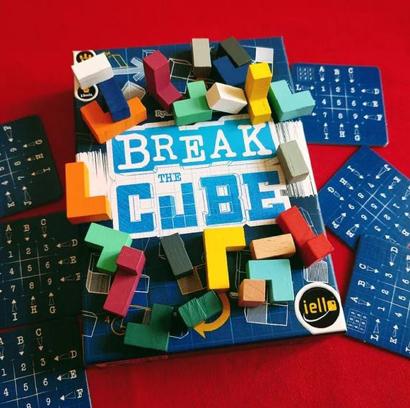 Break the Cube game by Iello, featuring a blue game box with the title prominently displayed in white and light blue letters. Colorful, geometric wooden pieces in various shapes and colors are scattered around the box, alongside game cards with letters and numbers on a blue background.