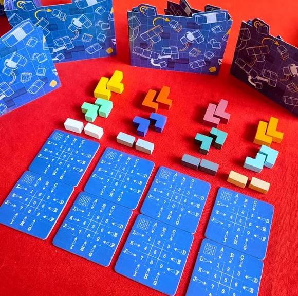 A colorful game setup for Break the Cube by Iello, featuring various geometric puzzle pieces in vibrant colors arranged alongside strategy cards on a red background. The game includes several uniquely shaped blocks, game boards with designs, and cards with numbers and symbols, encouraging creative problem-solving and teamwork.