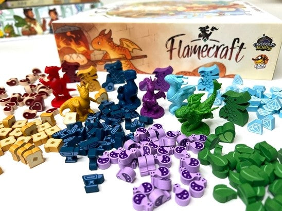 Flamecraft board game by Cardboard Academy Kickstarter featuring vibrant game pieces including colorful dragon miniatures, gems, and various tokens spread out beside the game box. The visual showcases a captivating collection of components designed for engaging gameplay.