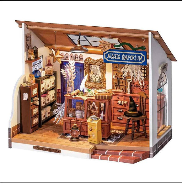 Kiki's Magic Emporium DIY kit featuring intricate wooden details, including a shelf filled with jars, a large wooden counter adorned with magical items, and decorative elements like a broom and a witch's hat. The charming emporium is designed to inspire creativity and imagination in crafting.