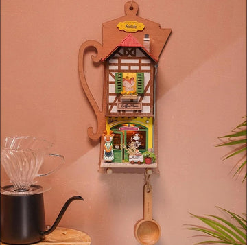 The Lazy Coffee House DIY kit by Robotime features an intricate wooden design resembling a coffee house. It showcases vibrant colors with a detailed exterior, including windows, a cheerful figure, and a miniature coffee shop scene. Perfect for craft enthusiasts, this maker kit offers a delightful hands-on experience, ideal for decoration or as a gift.