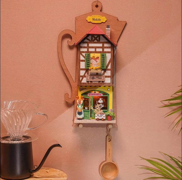 The Lazy Coffee House DIY kit by Robotime features an intricate wooden design resembling a coffee house. It showcases vibrant colors with a detailed exterior, including windows, a cheerful figure, and a miniature coffee shop scene. Perfect for craft enthusiasts, this maker kit offers a delightful hands-on experience, ideal for decoration or as a gift.