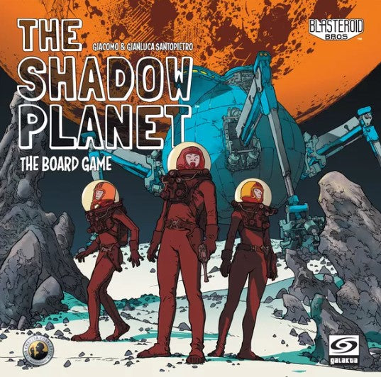 The Shadow Planet board game by Galakta features three astronauts in space suits standing on a rocky landscape. Behind them is a futuristic vehicle set against a vibrant orange planet. The title appears prominently at the top, with artwork showcasing a sci-fi theme and exploration elements.