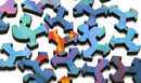 A collection of uniquely shaped jigsaw puzzle pieces from the Volcano#3 jigsaw puzzle by Grant Haffner, featuring vibrant colors and intricate designs. The pieces are made of high-quality wood, showcasing various shades of blue, green, orange, and purple, arranged in a scattered layout.