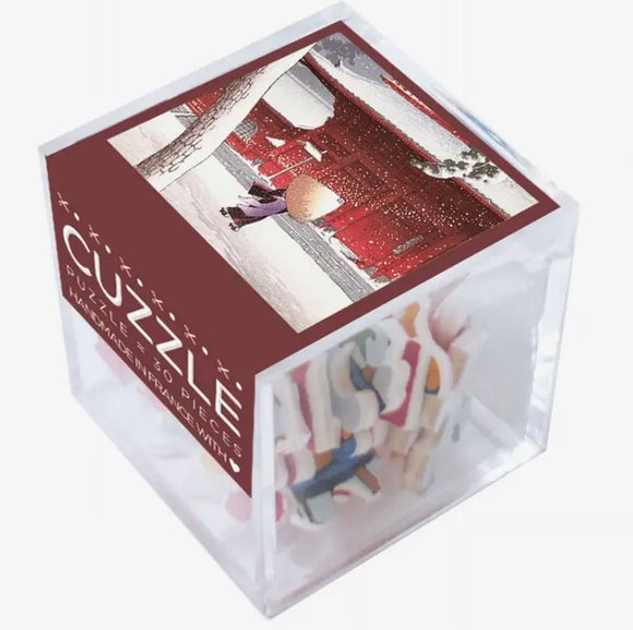 Cuzzle Zojoji jigsaw puzzle featuring a winter scene with a traditional red building and a figure holding an umbrella, packed in a clear cube. Contains 250 pieces.