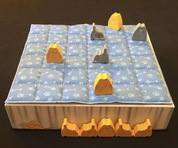 A game titled 'Boop.' by Smirk And Dagger. The game board is designed with a light blue quilted surface featuring paw prints and various colorful cat-themed tokens, including yellow and gray. The board is adorned with 3D elements resembling cats and rocks, creating a playful environment for an engaging gameplay experience.