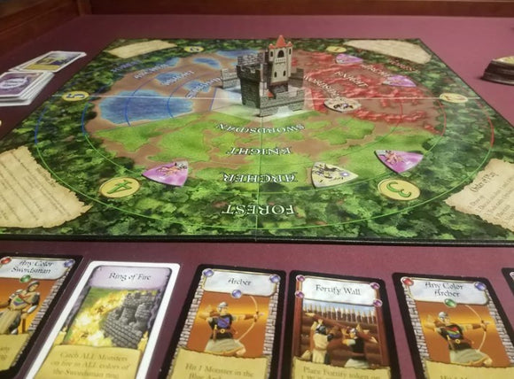 Castle Panic: 2nd Edition board game displayed on a table. The game features a circular game board with a castle in the center, surrounded by various colored sections representing monster paths. Several character cards lie beneath the board, showcasing different strategies, including 'Ring of Fire' and 'Archer.' The overall setting suggests a fantasy theme focused on defending the castle from approaching monsters.