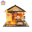 A detailed DIY miniature model of a charming autumn grocery store, showcasing various items like food jars, colorful goods, and decorative elements outside. The structure features bright yellow walls, a sloped roof, and a welcoming entrance adorned with signs and lanterns, perfect for craft enthusiasts looking to create a cozy scene.