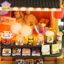 A detailed depiction of miniature grocery store items, showcasing vibrant colorful displays such as a smiling cat figurine, glass jars filled with candy and cotton, and small packets of snacks and drinks. The arrangement includes various food products and playful decorations, emphasizing a cozy autumn theme.